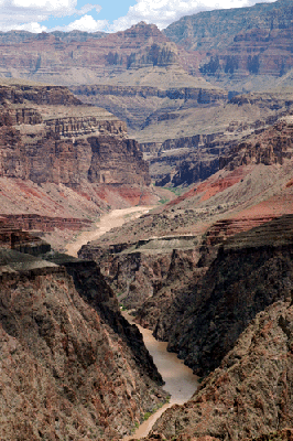 Looking upstream along the Colorado, a river raft in shadow at the nearest bend approaches Sockdolager Rapids