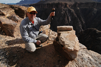 Dennis squats next to boulders used to anchor tram system used by 1919 survey to hoist supplies from the river to the Tonto level